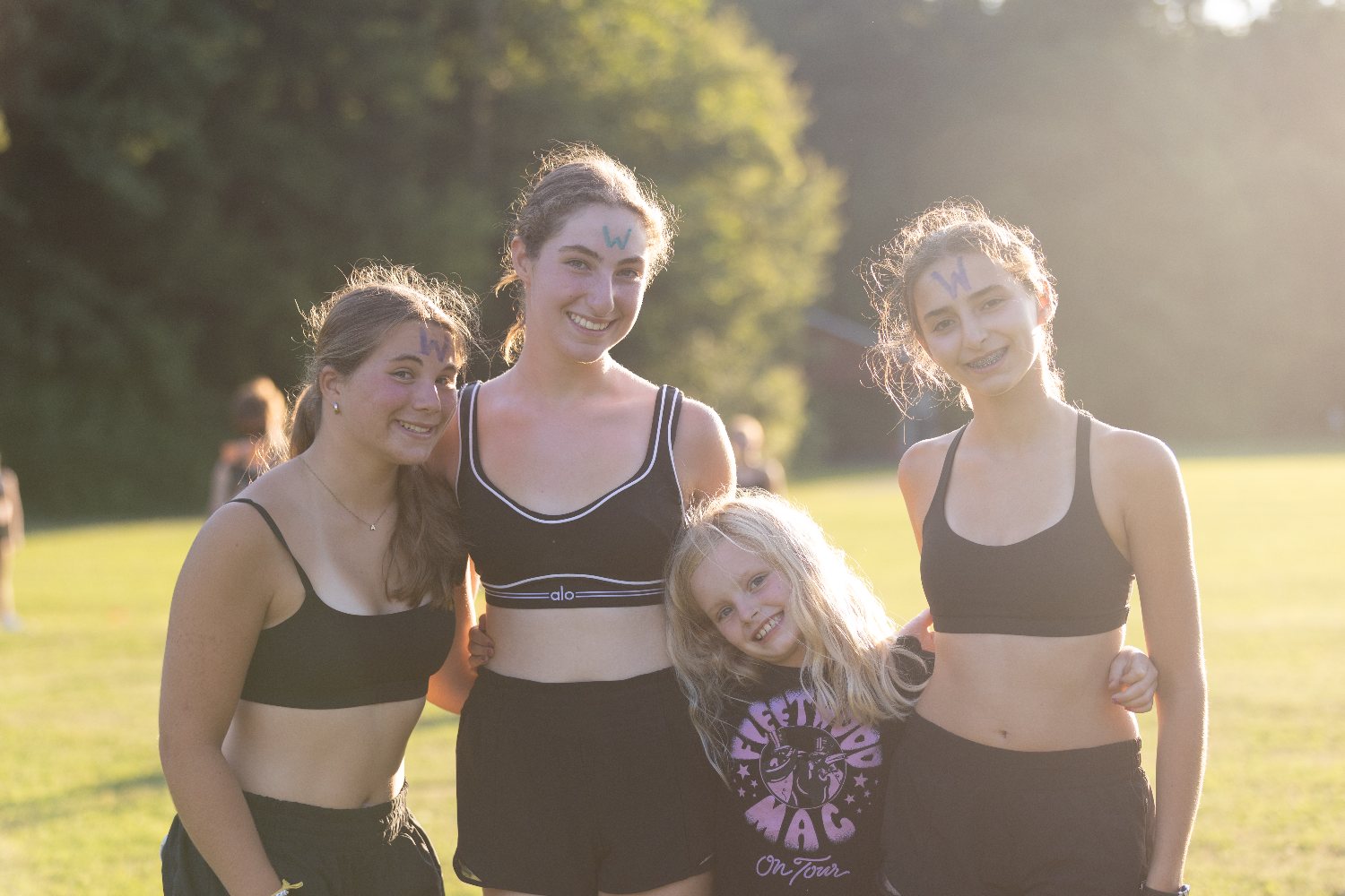 Four campers with painted faces standing together in golden-hour light