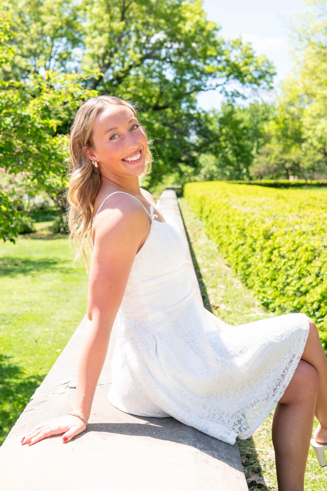 Woman in a white dress seated on a garden wall